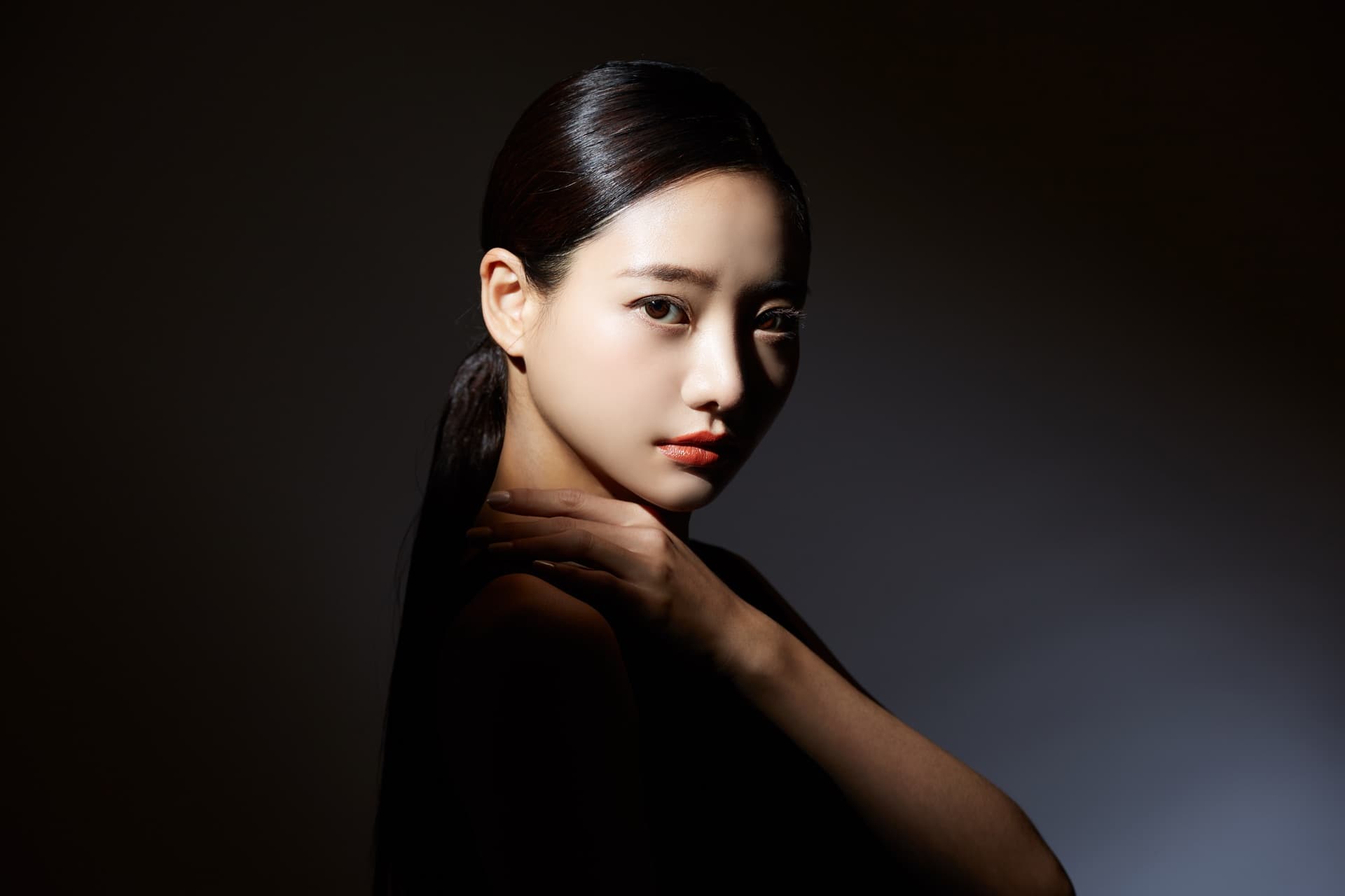暗調戲劇光下的東方女性側顏,手輕撫頸肩,象徵不同年齡階段的肌膚養護節奏