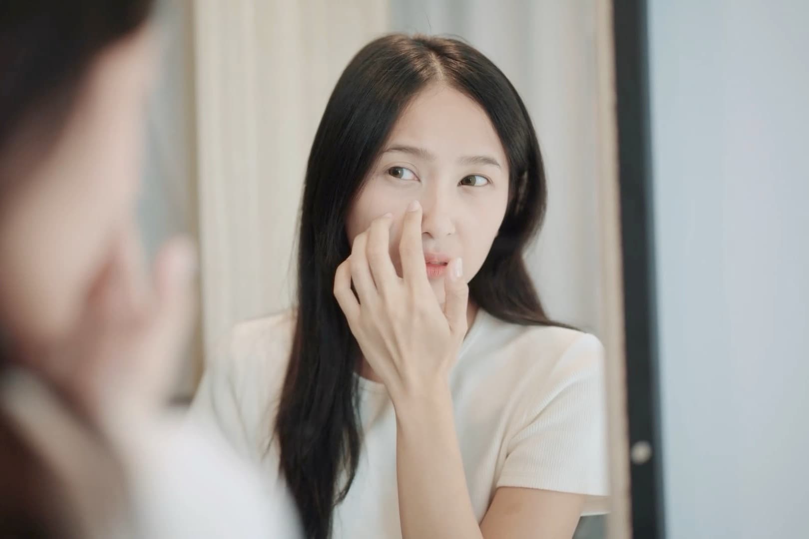 女子在鏡前以指尖端詳自己的膚況,觀察先於行動